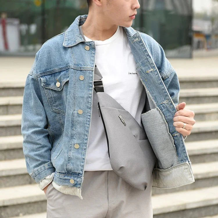 Young man wearing denim jacket and white t-shirt with gray crossbody sling bag outdoors