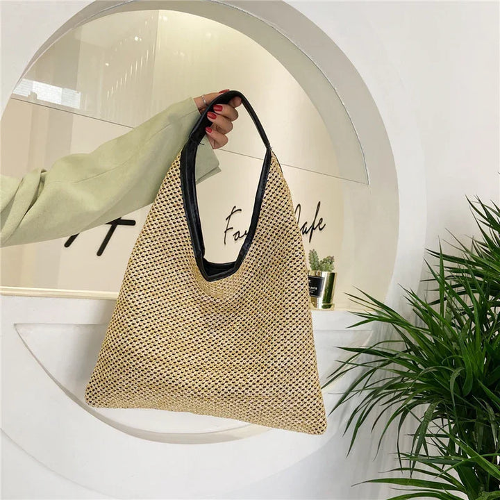 Hand holding a stylish beige woven tote bag with black handle in modern cafe interior