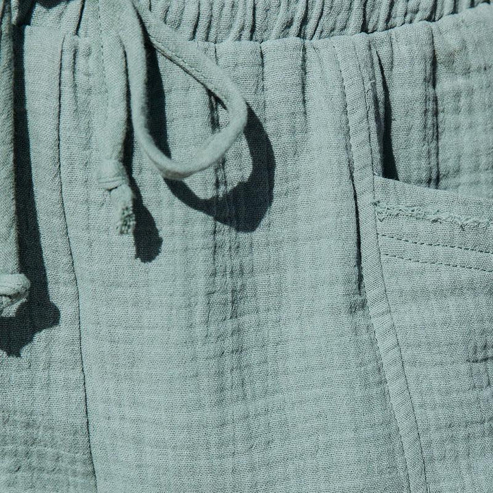 Close-up of light blue textured fabric pants with drawstring and visible side pocket stitching