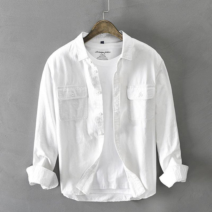 white casual shirt with two chest pockets hanging on wooden hanger against gray wall