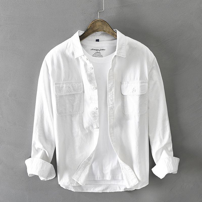 White casual button-up shirt with chest pockets and rolled sleeves on wooden hanger against gray wall