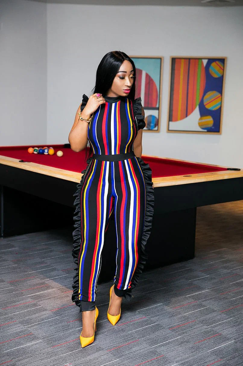Woman posing by pool table wearing a colorful striped jumpsuit with black ruffle details and yellow heels