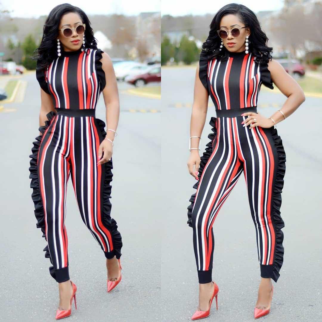 Woman wearing striped black, red, and white ruffled jumpsuit with red heels and sunglasses outdoors