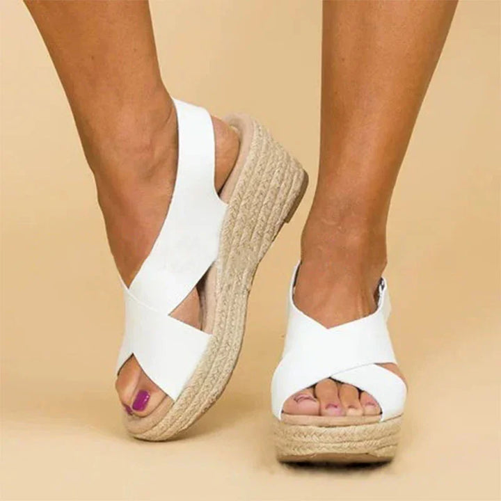 White wedge sandals with crisscross straps and jute platform sole on model's feet