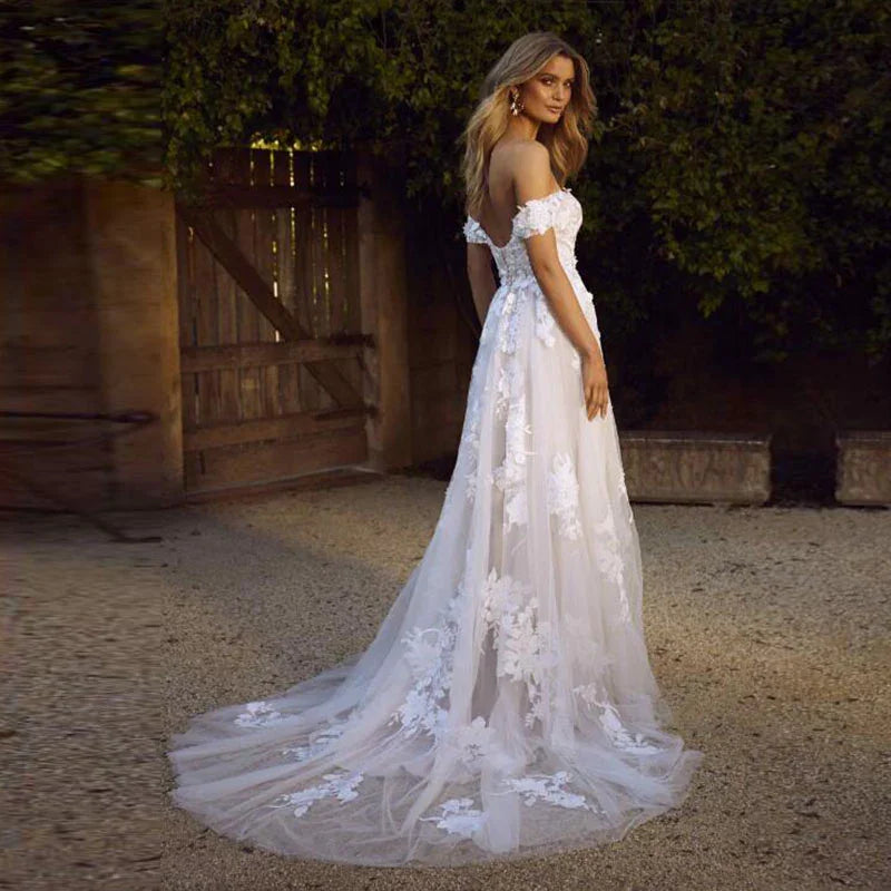 Bride wearing an off-shoulder lace wedding dress with floral applique train in outdoor garden setting