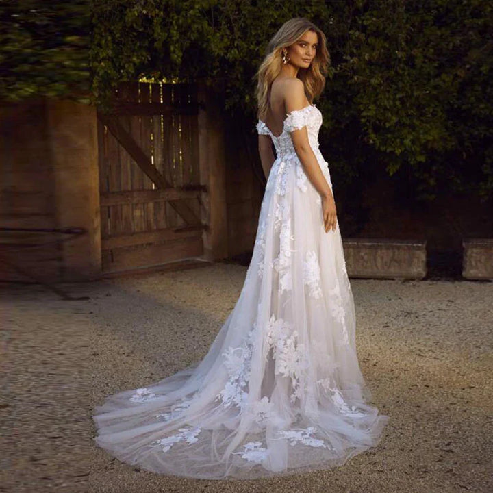 Bride wearing an off-shoulder lace wedding dress with floral applique train in outdoor garden setting