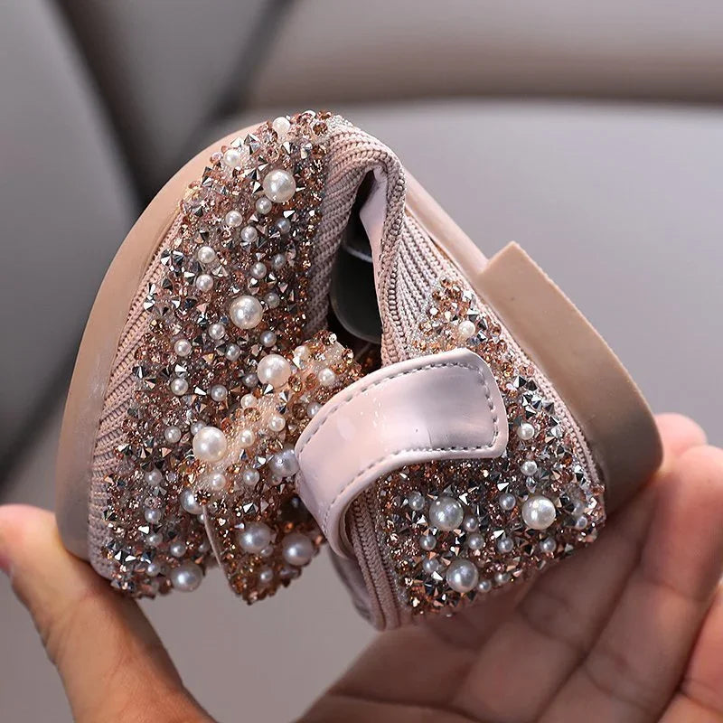 Flexible pink toddler shoe embellished with pearls and rhinestones held in hand