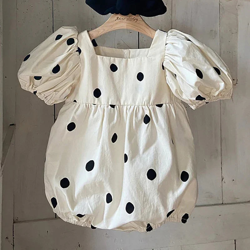 White baby romper with black polka dots and puff sleeves hanging on wooden hanger