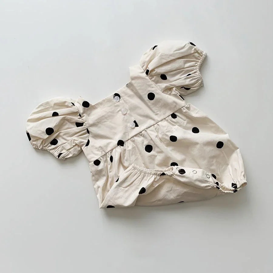 Cream baby romper with black polka dots and puff sleeves on a white background