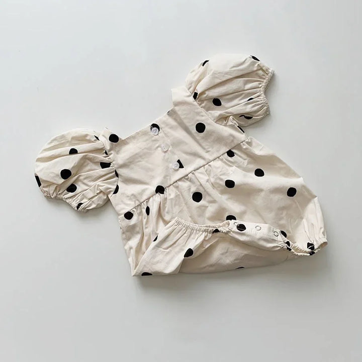 Cream baby romper with black polka dots and puff sleeves on a white background