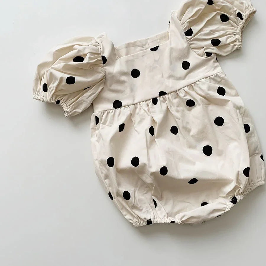 Cream baby romper with black polka dots and puff sleeves on white background