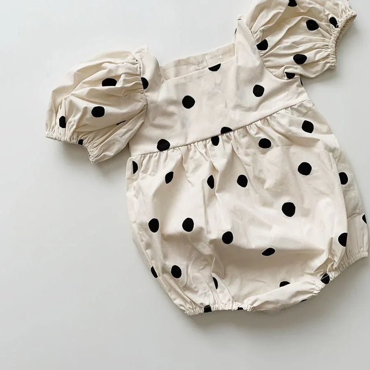 Cream baby romper with black polka dots and puff sleeves on white background
