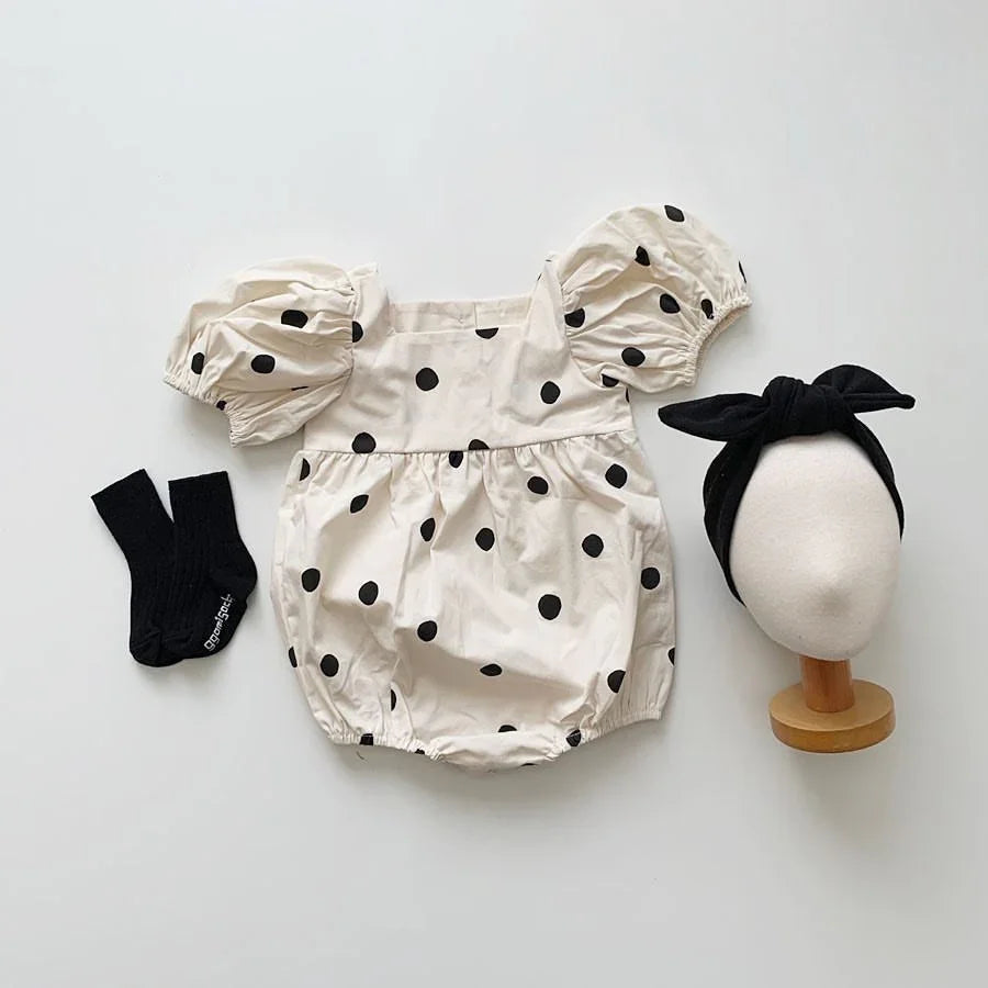 Cream toddler romper with black polka dots and puff sleeves, black socks, and black headband on mannequin