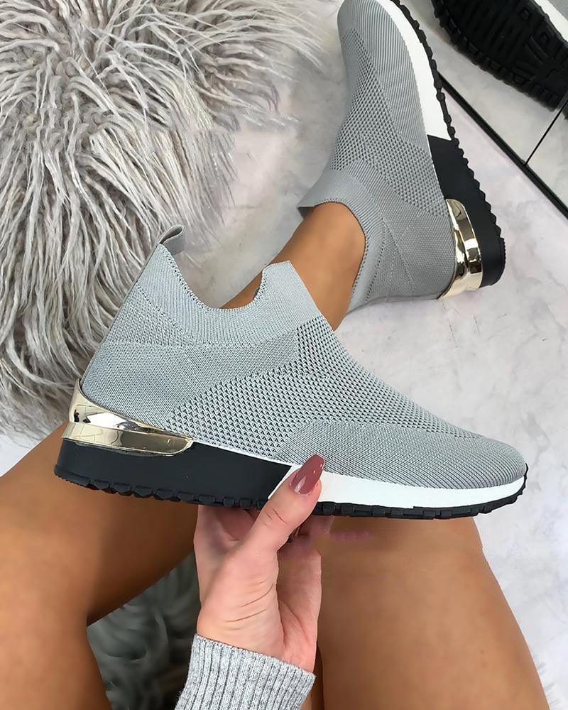 Light gray knitted slip-on sneakers with black and white sole and gold heel detail worn on legs with taupe skin tone