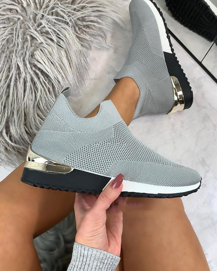 Light gray knitted slip-on sneakers with black and white sole and gold heel detail worn on legs with taupe skin tone