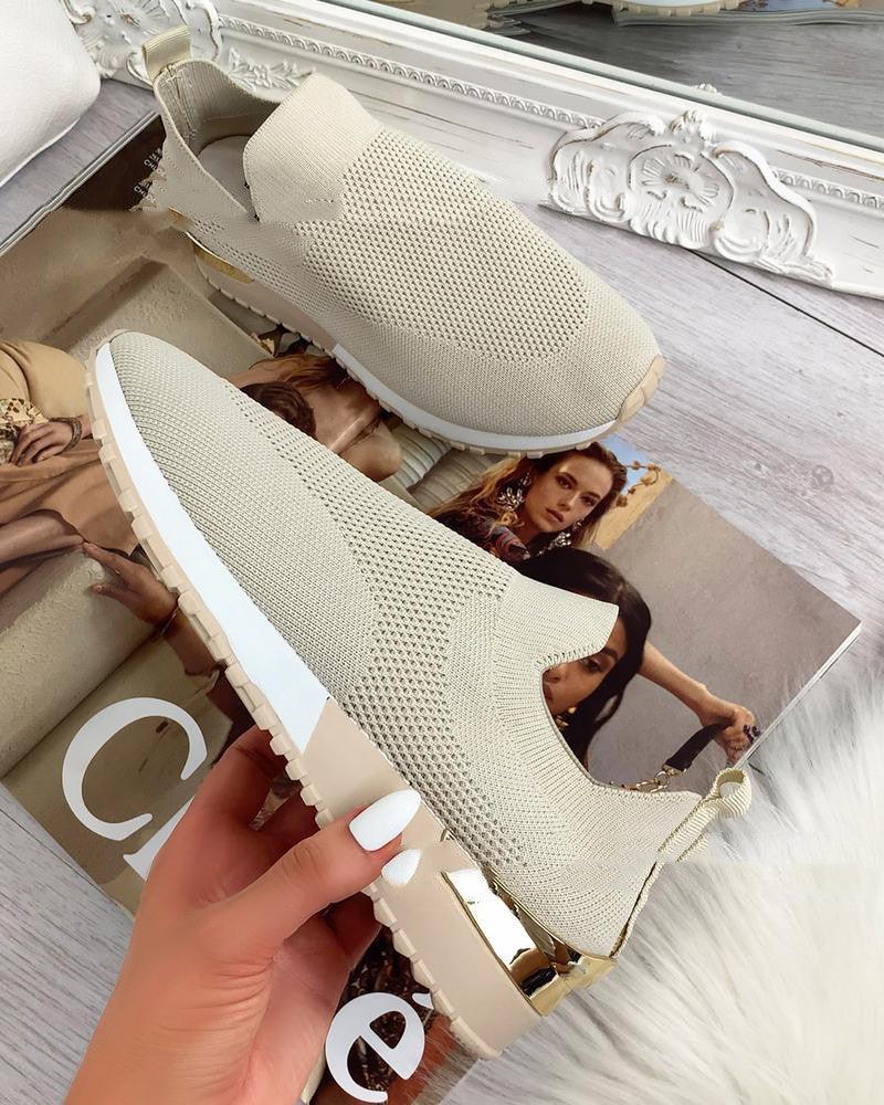 Pair of beige knitted slip-on sneakers with white soles and gold heel accents displayed on fashion magazine