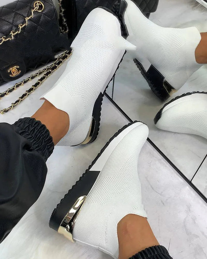 White knit sock sneakers with black soles and gold heel detail worn with black jogger pants on marble floor