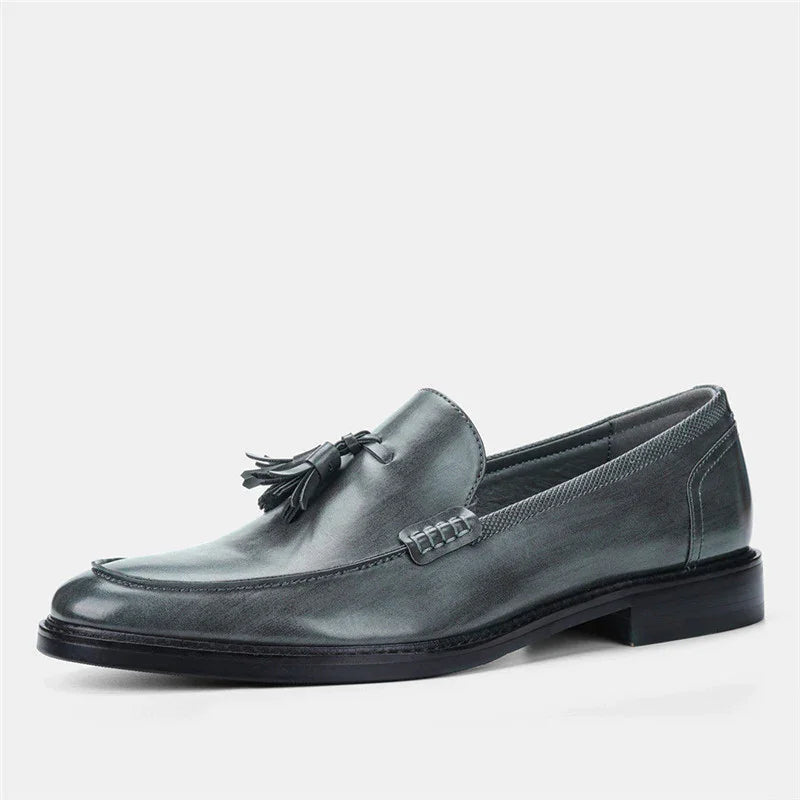 Gray leather men's tassel loafer with stitched accents and low heel on white background