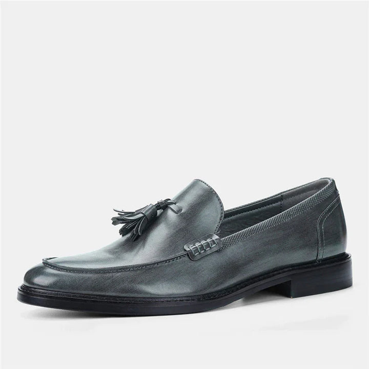 Gray leather men's tassel loafer with stitched accents and low heel on white background