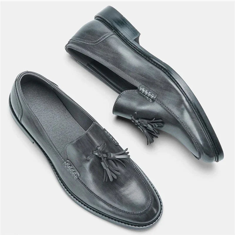 Black leather men's tassel loafers with stitched detailing on a white background