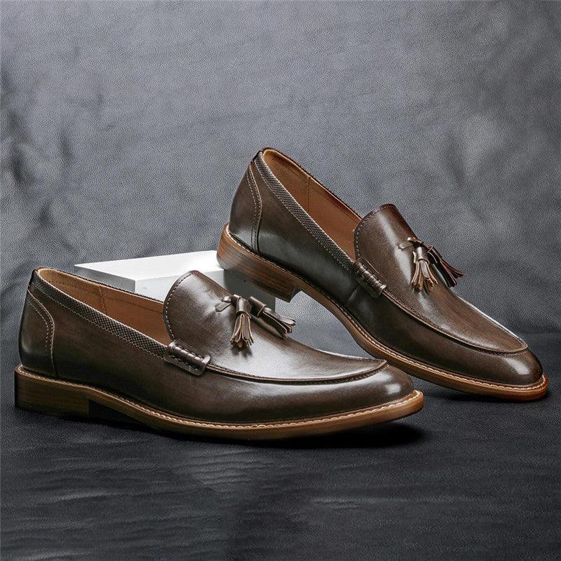 Pair of brown leather tassel loafers with tan soles displayed on dark surface against gray background