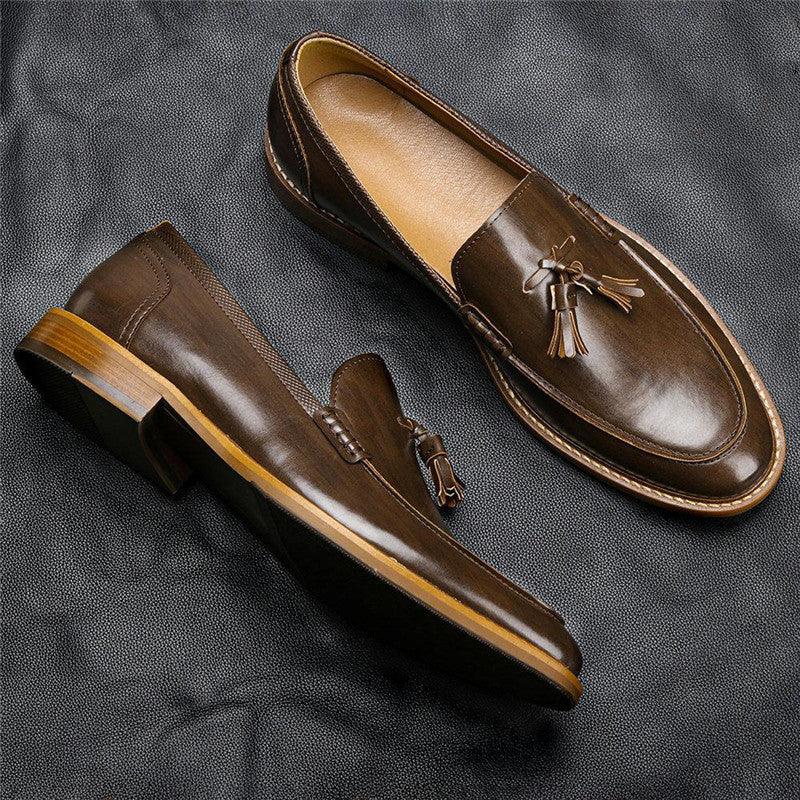Pair of brown leather tassel loafers on black textured surface with wooden heels