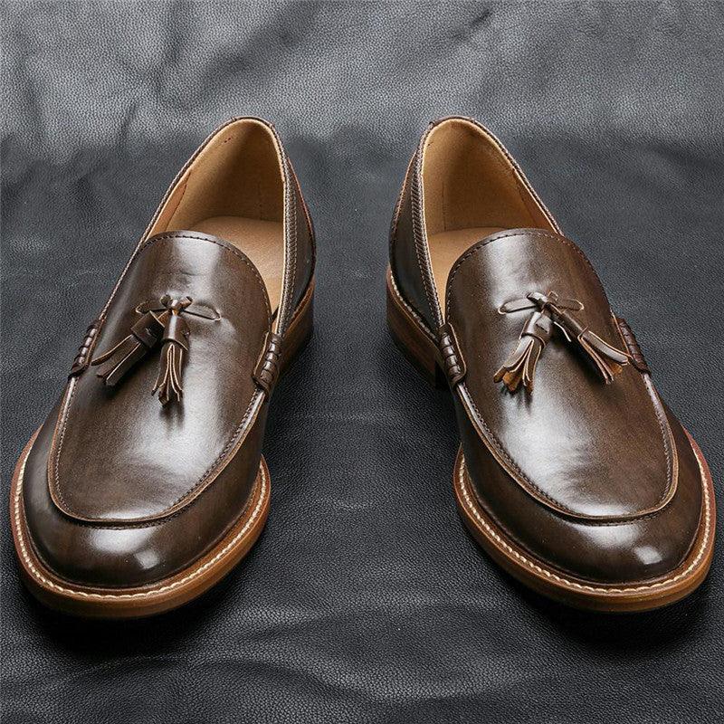 Pair of brown leather tassel loafers on black textured surface, classic men's dress shoes