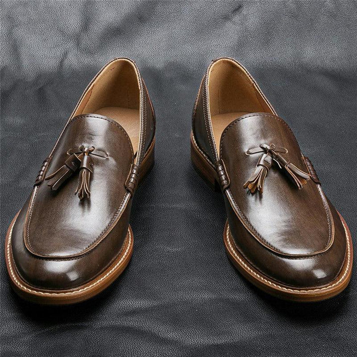 Pair of brown leather tassel loafers on black textured surface, classic men's dress shoes