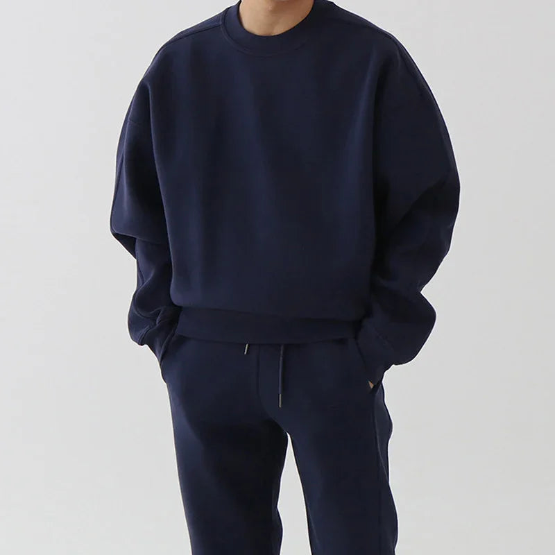 Man wearing a navy blue sweatshirt and matching sweatpants with hands in pockets