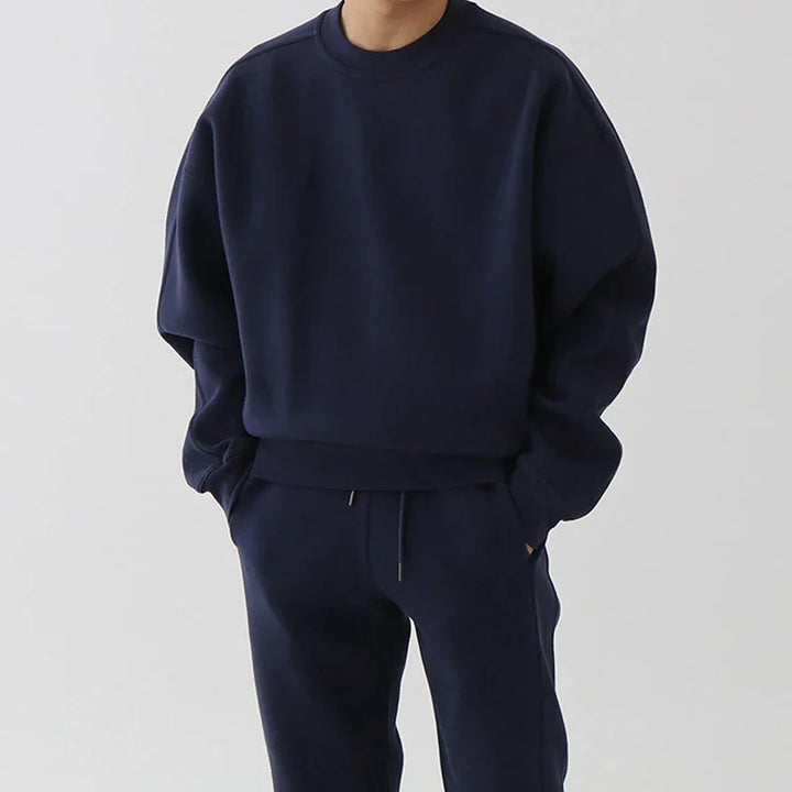 Man wearing a navy blue sweatshirt and matching sweatpants with hands in pockets