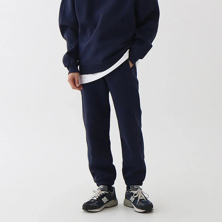 person wearing navy blue sweatpants with cuffed ankles and navy blue sneakers on white background