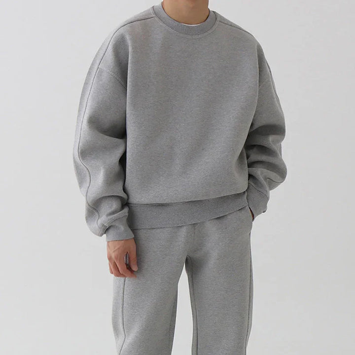 Person wearing casual grey sweatshirt and matching sweatpants with relaxed fit on light background