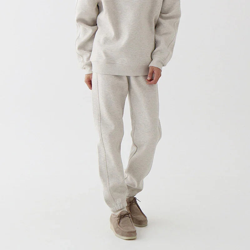 Close-up of person wearing beige sweatpants and matching sweatshirt with brown casual shoes on white background
