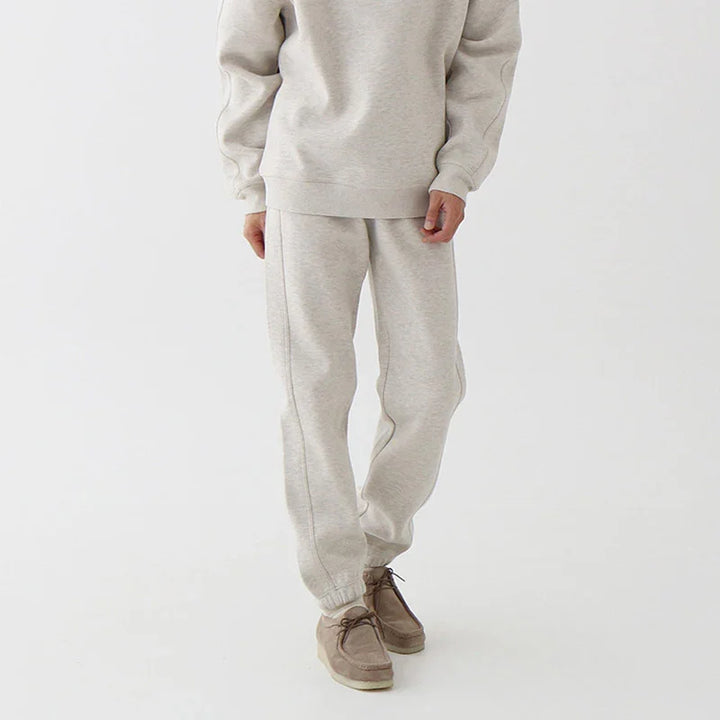 Close-up of person wearing beige sweatpants and matching sweatshirt with brown casual shoes on white background