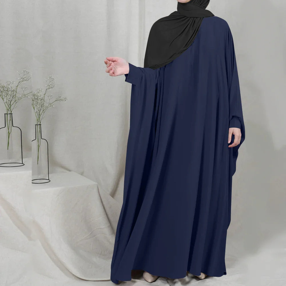 Woman wearing a navy blue abaya and black hijab standing indoors with minimalistic floral decor