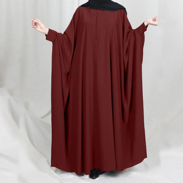 Back view of a woman wearing a loose maroon abaya with wide sleeves and a black hijab