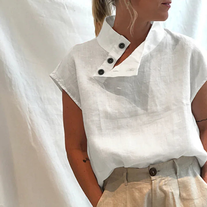 Woman wearing a white sleeveless linen top with an asymmetrical buttoned collar and beige trousers