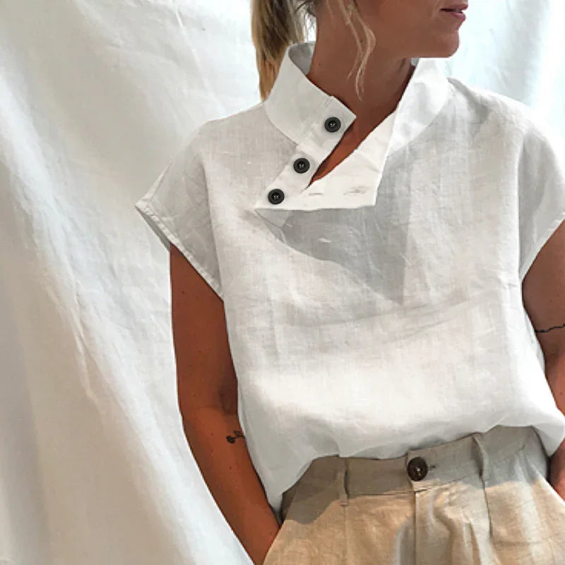 Woman wearing white linen short sleeve top with buttoned high collar and beige pants