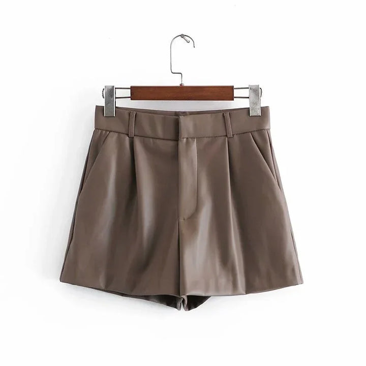 Brown faux leather high-waisted shorts with front pleats hanging on wooden hanger