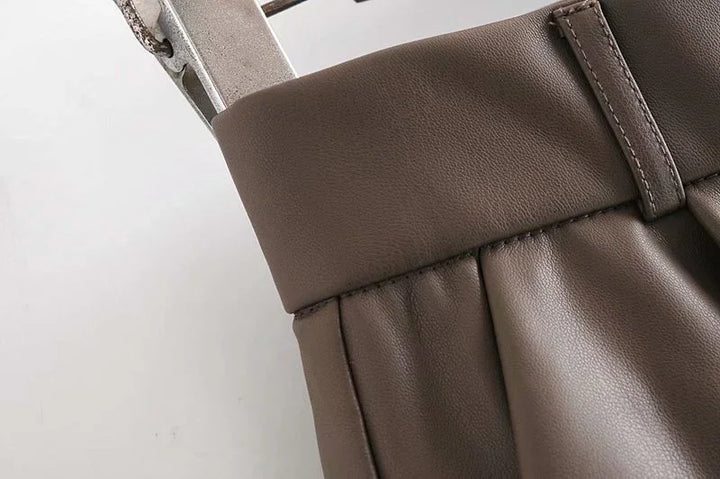 Close-up of brown faux leather skirt waistband and pleats on a white background