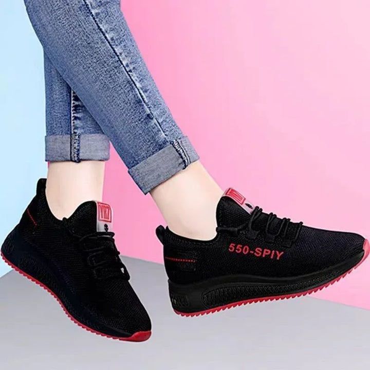 Black sneakers with red accents and 550-SPY text worn with rolled blue jeans against pink background