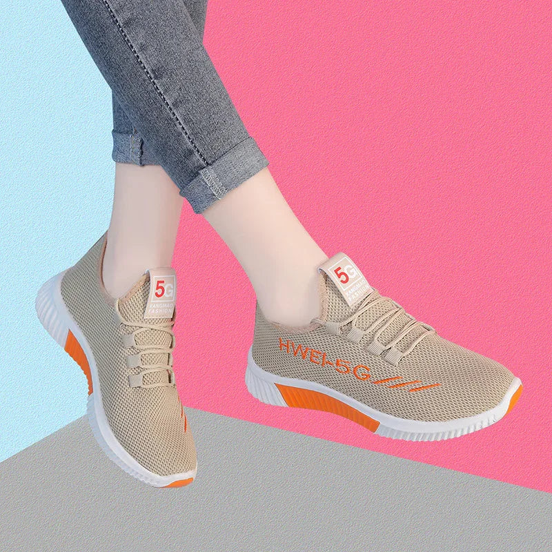 Beige mesh sneakers with orange accents and white soles worn with gray rolled-up jeans on colorful background