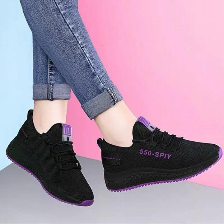 Black and purple casual sport sneakers with 550 SPIY text, worn with rolled-up blue jeans against pink background