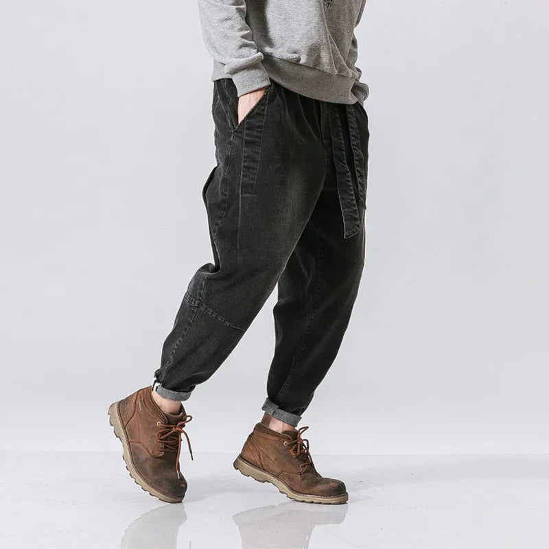 Person wearing black casual jogger pants and brown lace-up boots on gray background