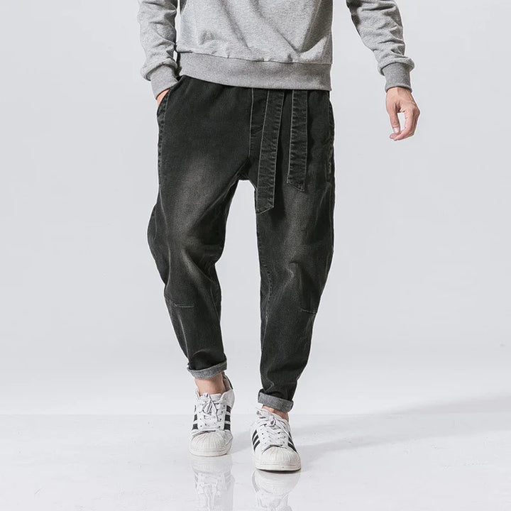 Man wearing black casual jogger pants with drawstring and cuffed hems paired with white sneakers and grey sweatshirt
