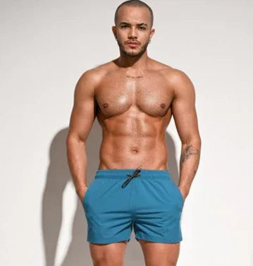 Muscular shirtless man wearing blue swim shorts posing against plain light background