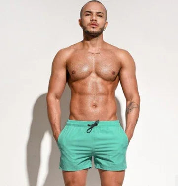 Muscular man wearing green swim shorts standing against plain white background