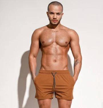 Muscular man modeling brown swim shorts against plain white background