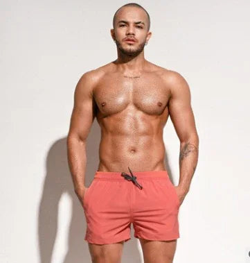 muscular man wearing red swim shorts standing against plain light background