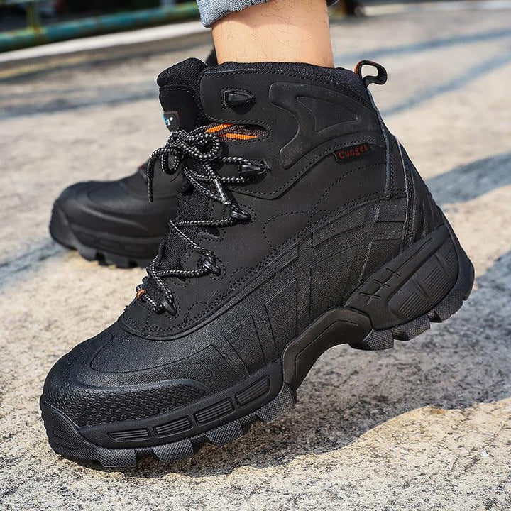 Black rugged hiking boots with textured soles worn outdoors on concrete surface